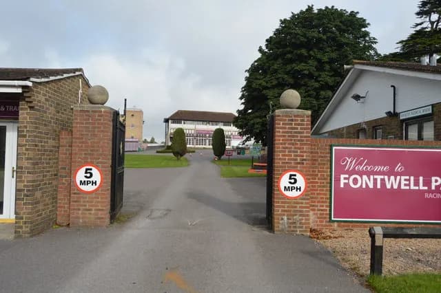 The entrance to Fontwell Park Racing with two brick pillars, speed limit signs, and a welcome sign, leading to buildings and green lawns.