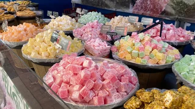 A vibrant assortment of Turkish delight in various colors like pink, yellow, orange, and green, displayed in numerous large trays on a market stall.