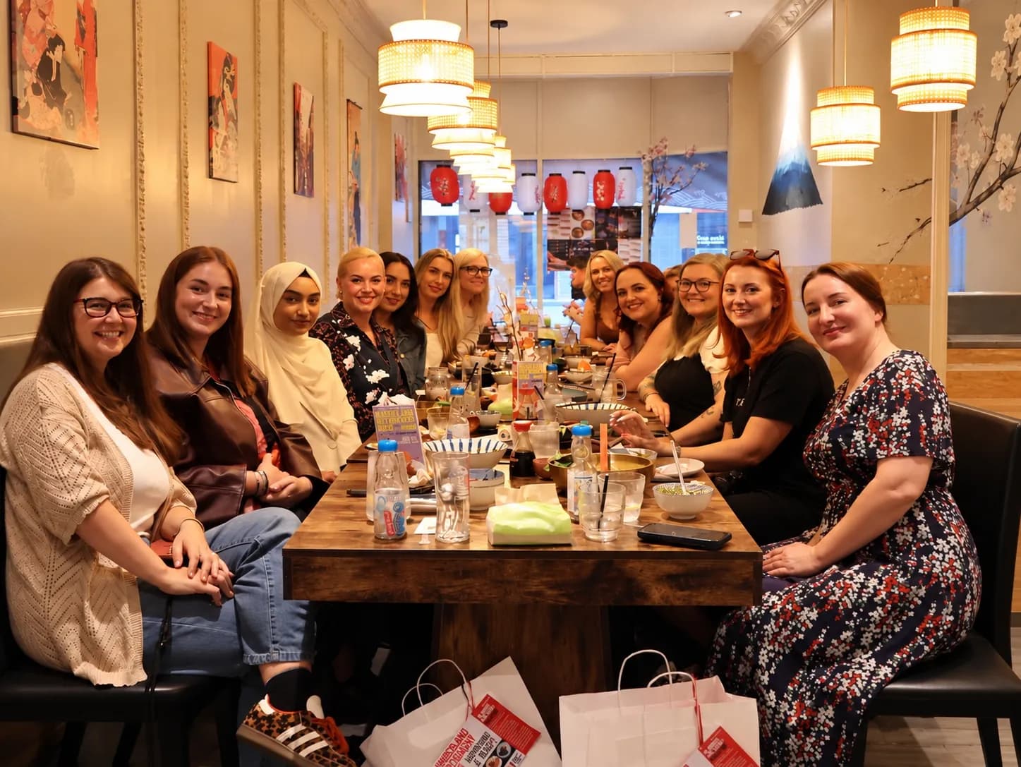 A group of women are seated around a long table in a restaurant, smiling towards the camera.