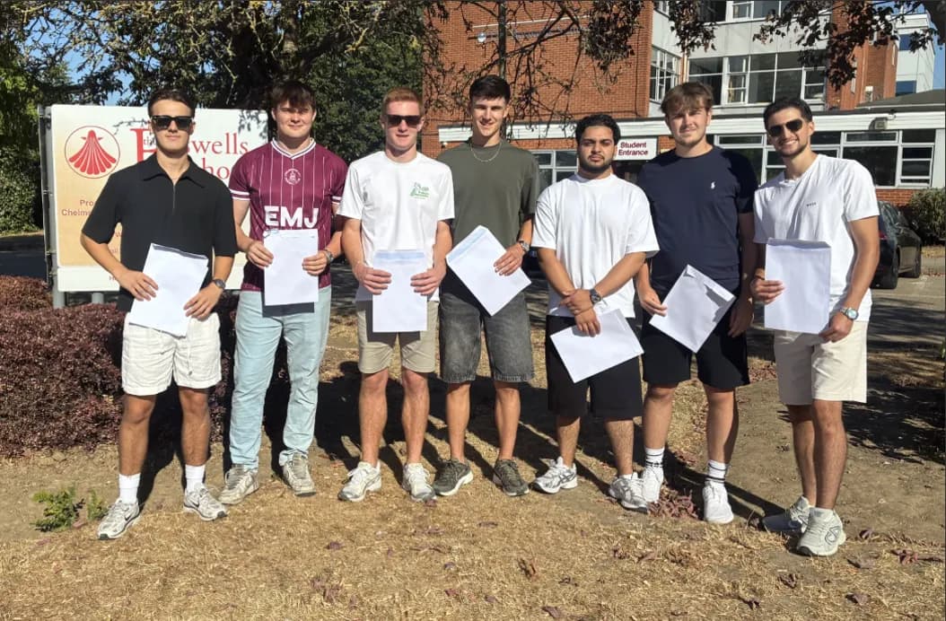 Seven young men, smiling and holding envelopes, stand outside a building with a sign that reads "Howells School."