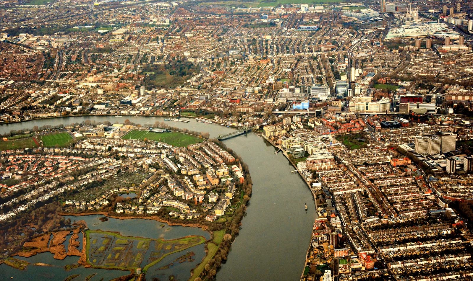 An aerial view of a densely populated city with a winding river flowing through it, separating residential areas from commercial and industrial zones.