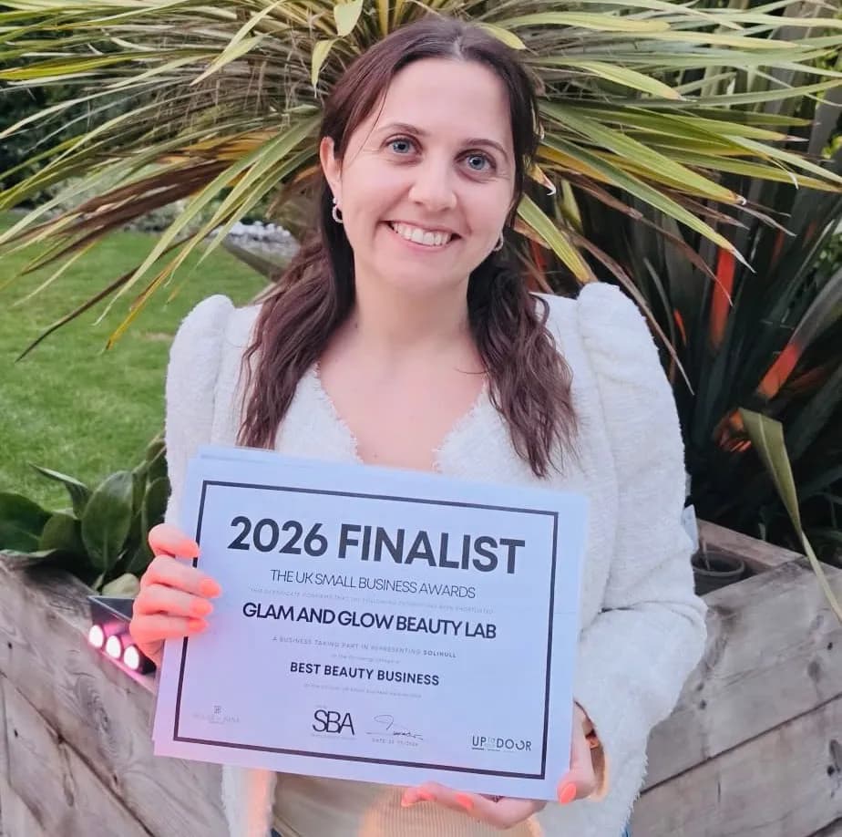 A smiling woman with dark hair holds up a certificate that reads "2026 FINALIST THE UK SMALL BUSINESS AWARDS GLAM AND GLOW BEAUTY LAB BEST BEAUTY BUSINESS."