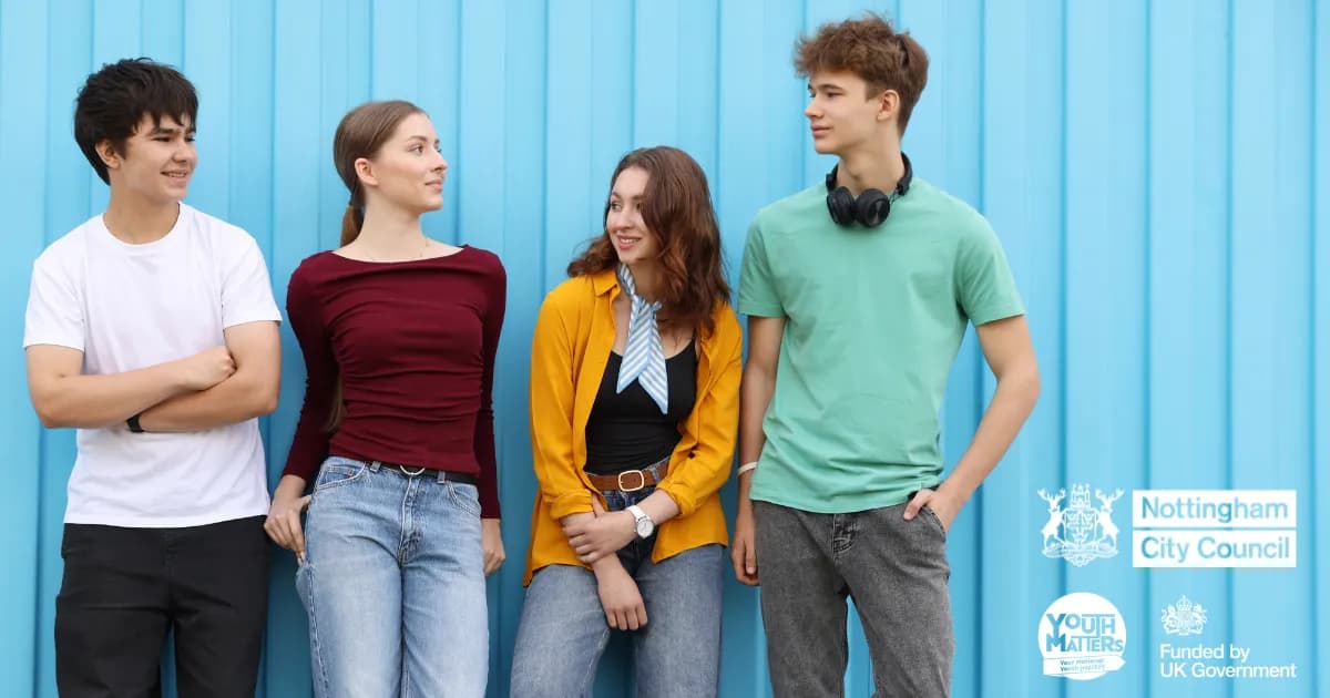 Four young people, two males and two females, standing casually in front of a bright blue wall, looking in different directions.