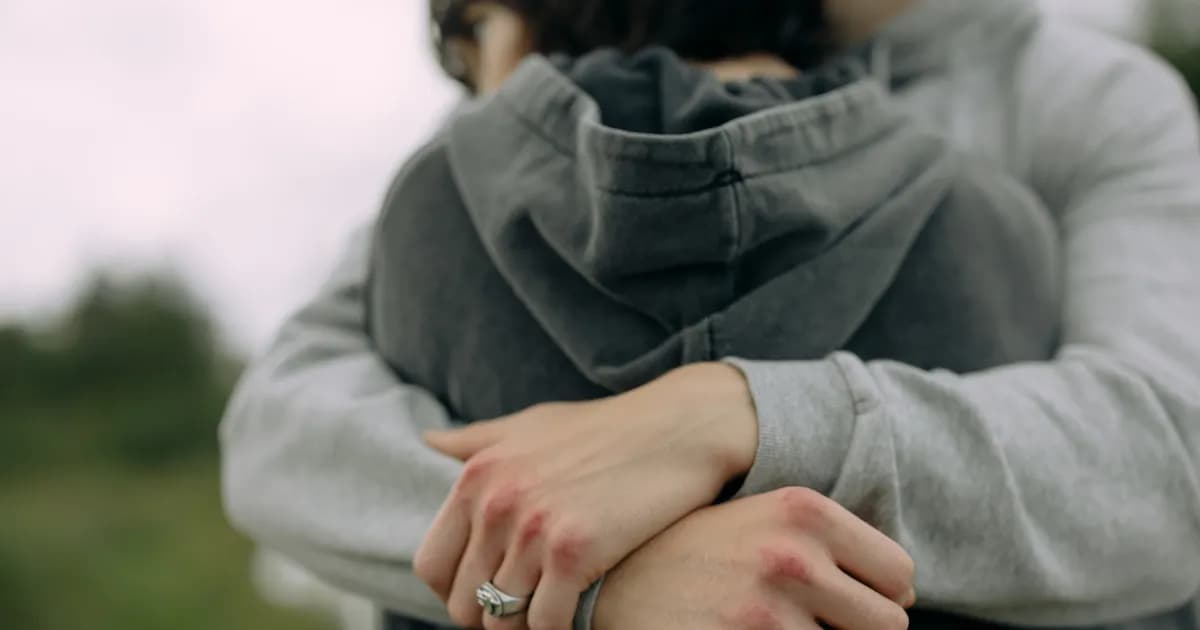 Two people embracing, with one person's arms wrapped around the other's back, focusing on the hands.
