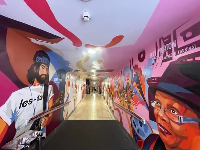 A long, bright hallway with colorful murals painted on the walls and ceiling, featuring portraits of people and abstract shapes.