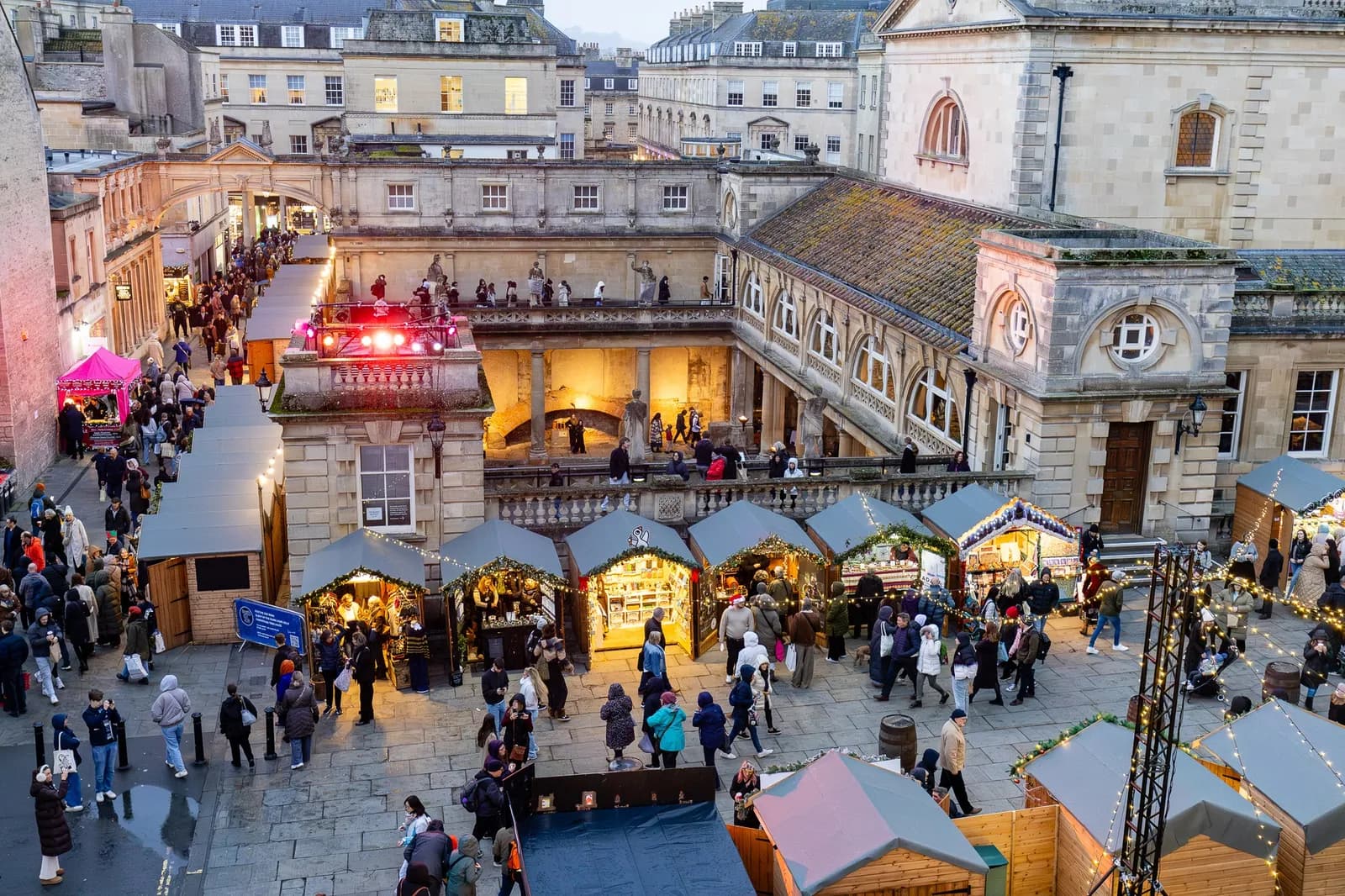 An aerial view of the Bath Christmas market with numerous stalls and people walking around an old stone building.