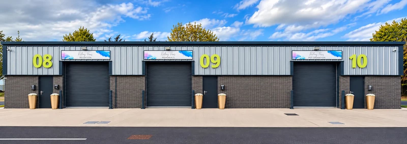 A modern light industrial building with three grey roller doors, each with a bright sign above and a door next to it, and large numbers 08, 09, and 10 on the facade under a partly cloudy sky.