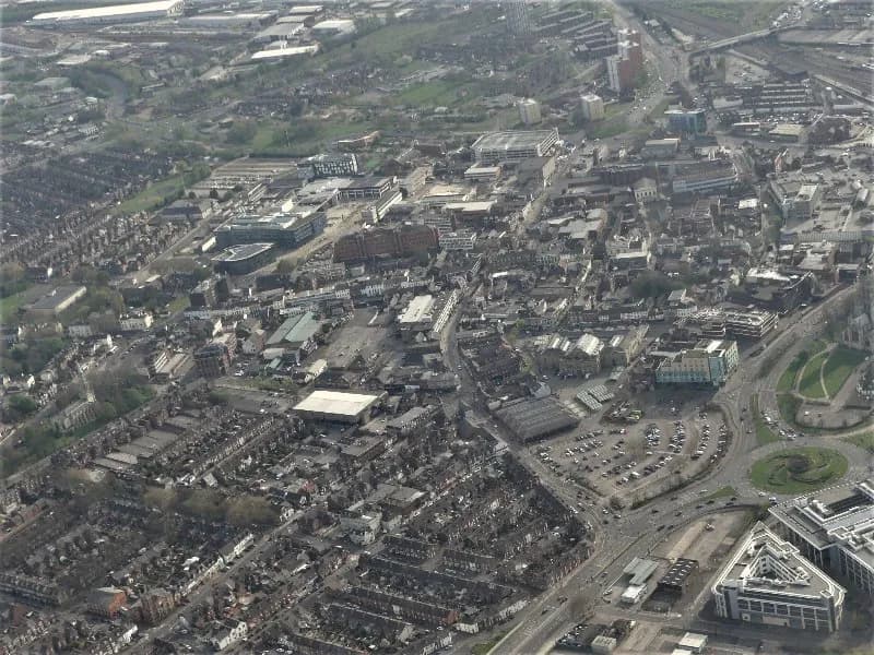 An aerial view captures a sprawling urban landscape featuring residential areas, commercial buildings, roads, and a large roundabout.
