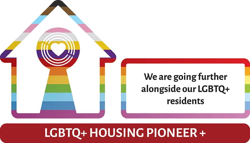 A house outline filled with rainbow and progress pride flag colors, featuring a keyhole with a heart at its center, alongside a red-bordered box containing the text 'We are going further alongside our LGBTQ+ residents', and a red banner below reading 'LGBTQ+ HOUSING PIONEER +'.