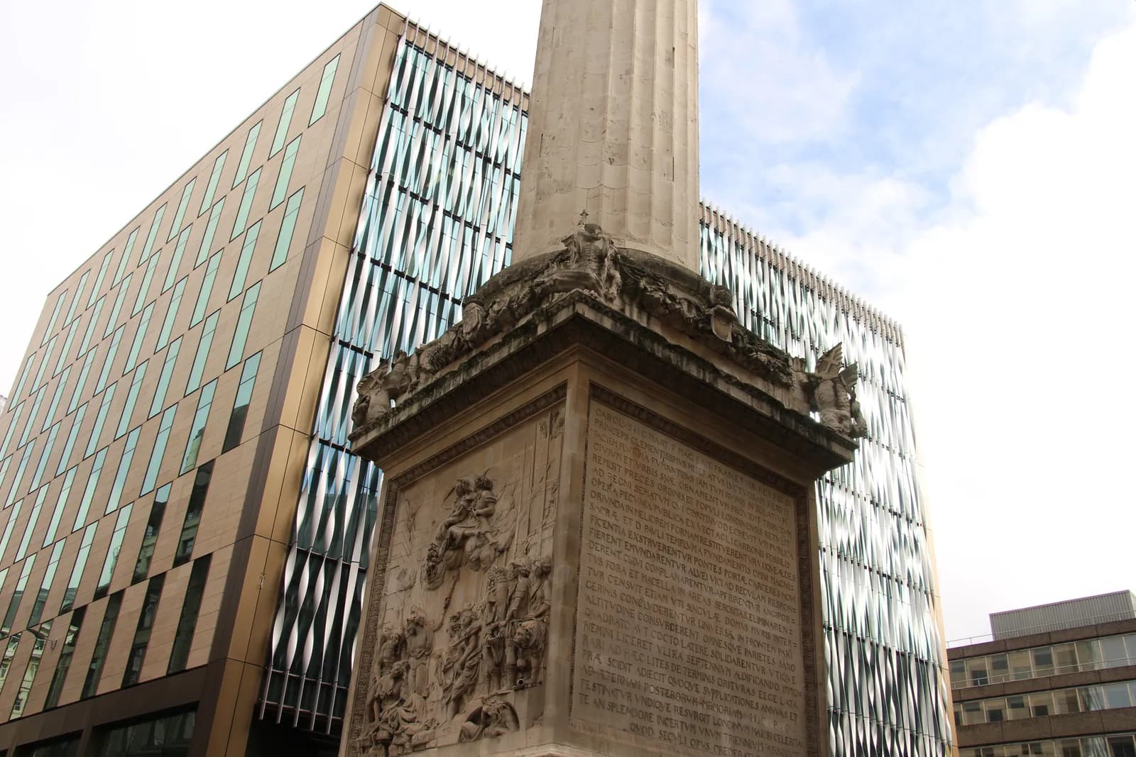 A towering stone monument with carved details and text stands in front of a modern building with a patterned reflective facade.