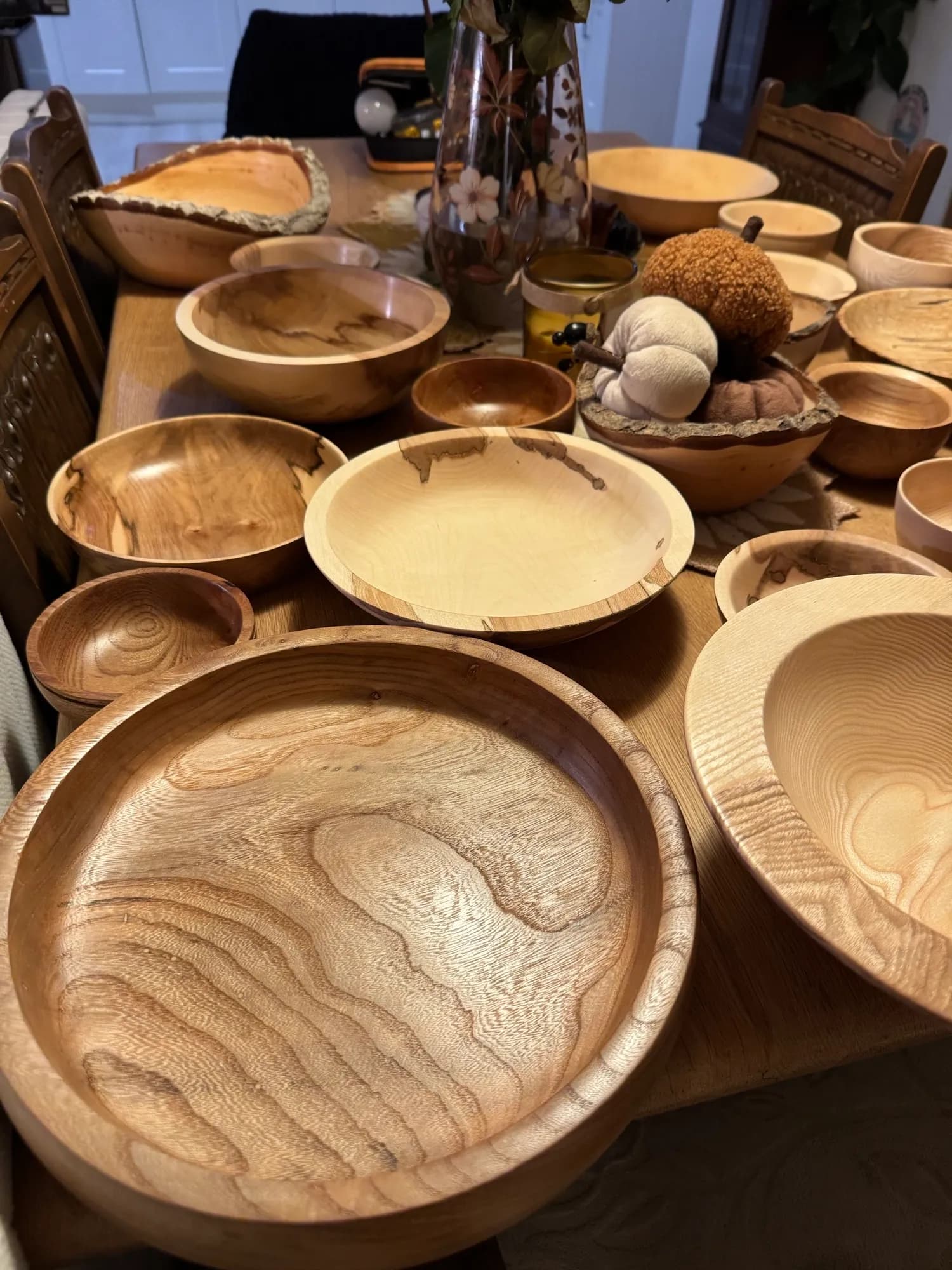 A table full of wooden bowls and carved items, including a centerpiece of decorative pumpkins and a vase with flowers.