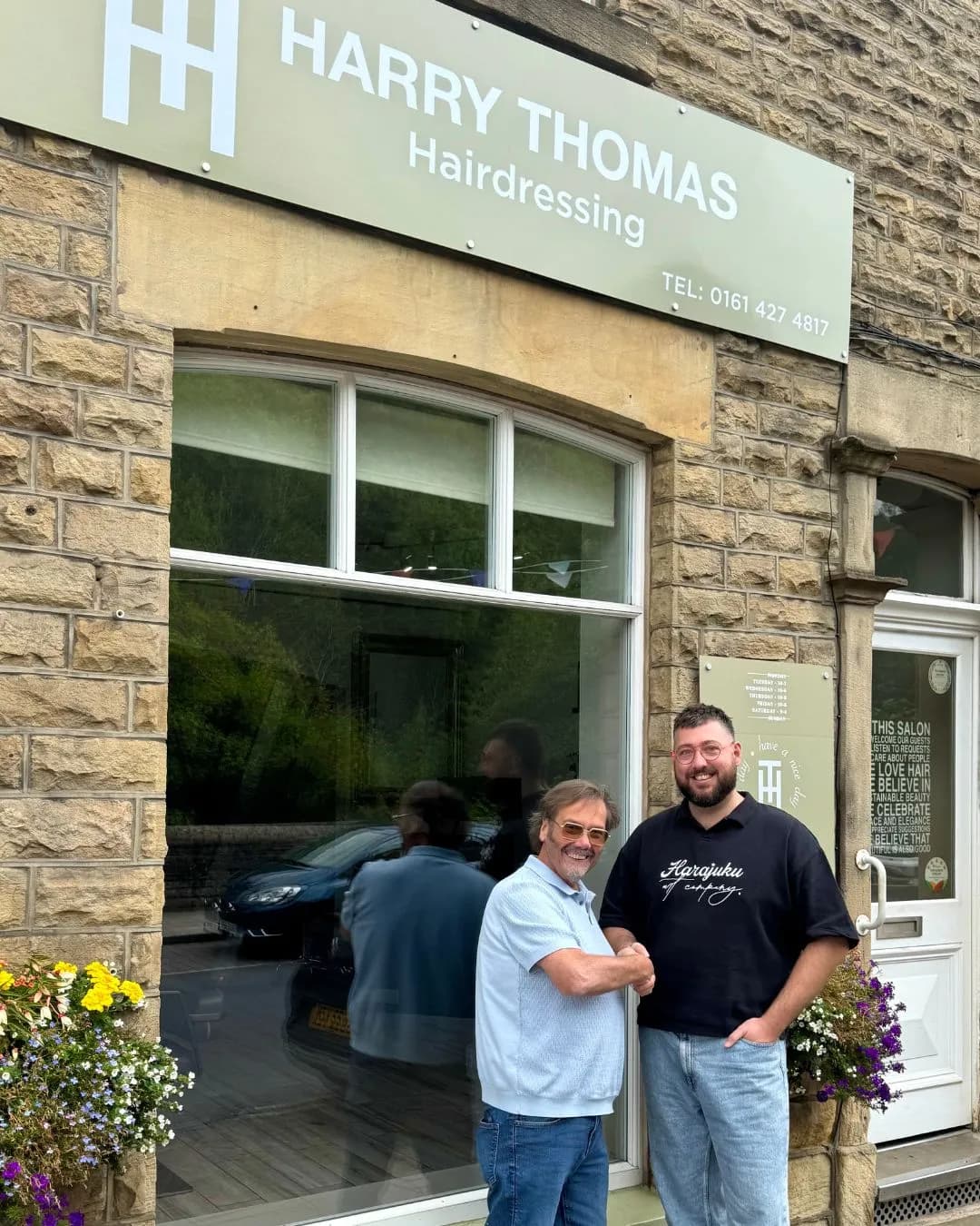 Two men shake hands in front of the Harry Thomas Hairdressing salon, with one man smiling at the camera and the other looking at his companion.