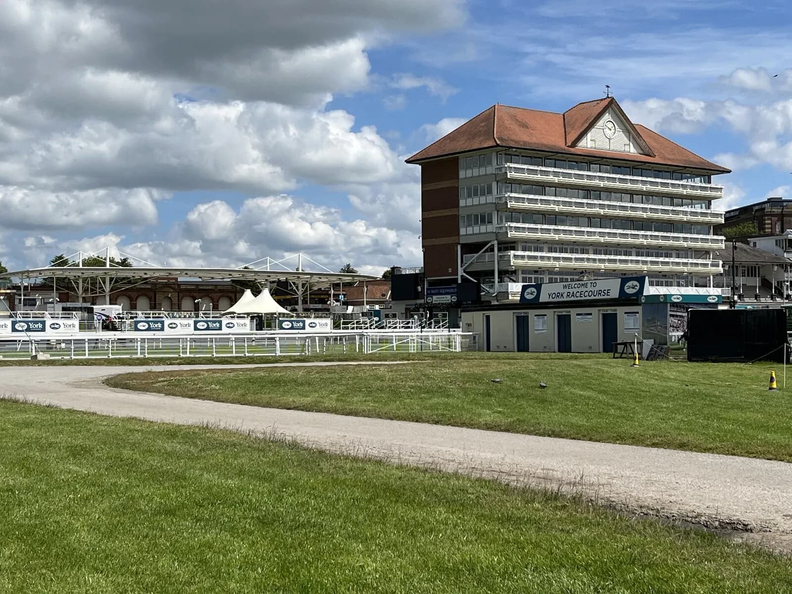 A view of the York Racecourse with a large building on the right and a track in the foreground, under a partly cloudy sky.
