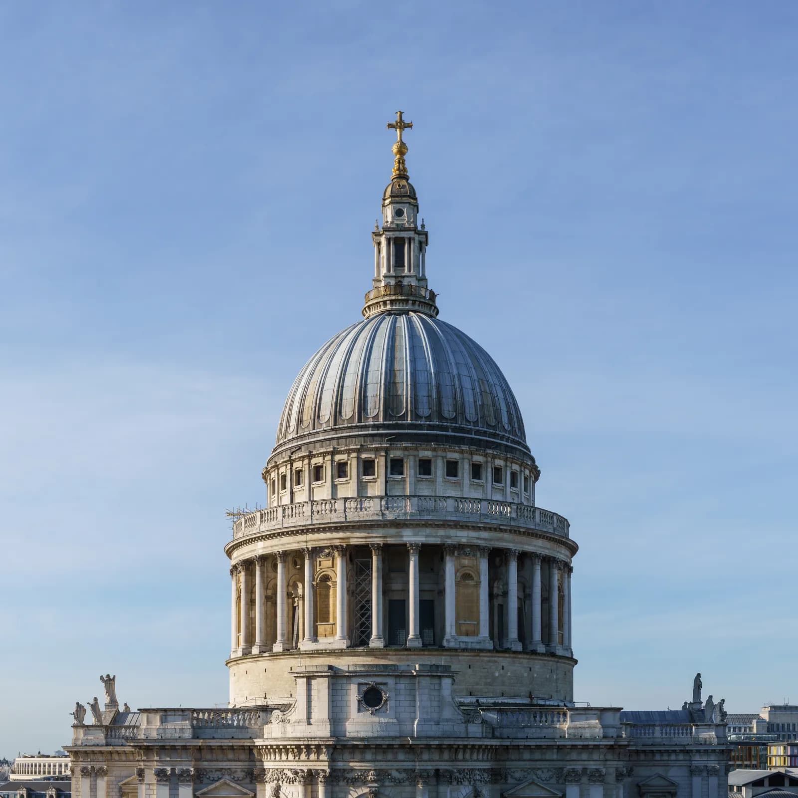 A close-up view of the majestic dome and golden cross finial of St. Paul's Cathedral against a clear blue sky.