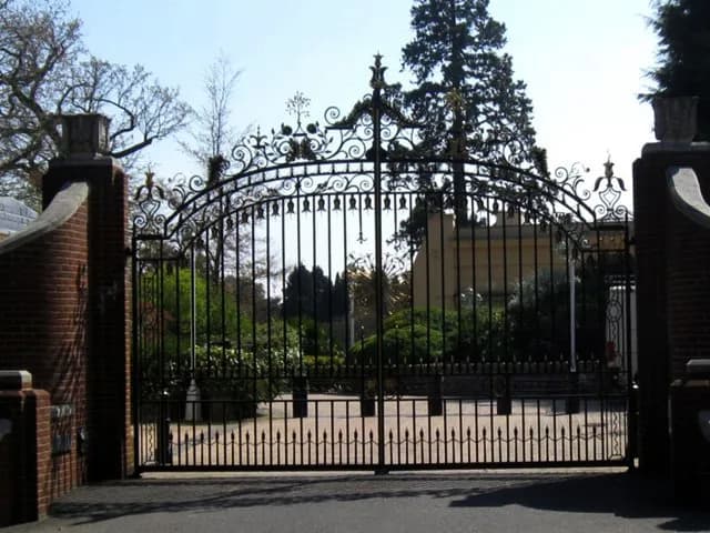 A sophisticated wrought iron gate, adorned with intricate scrollwork and finials, stands between two brick pillars.