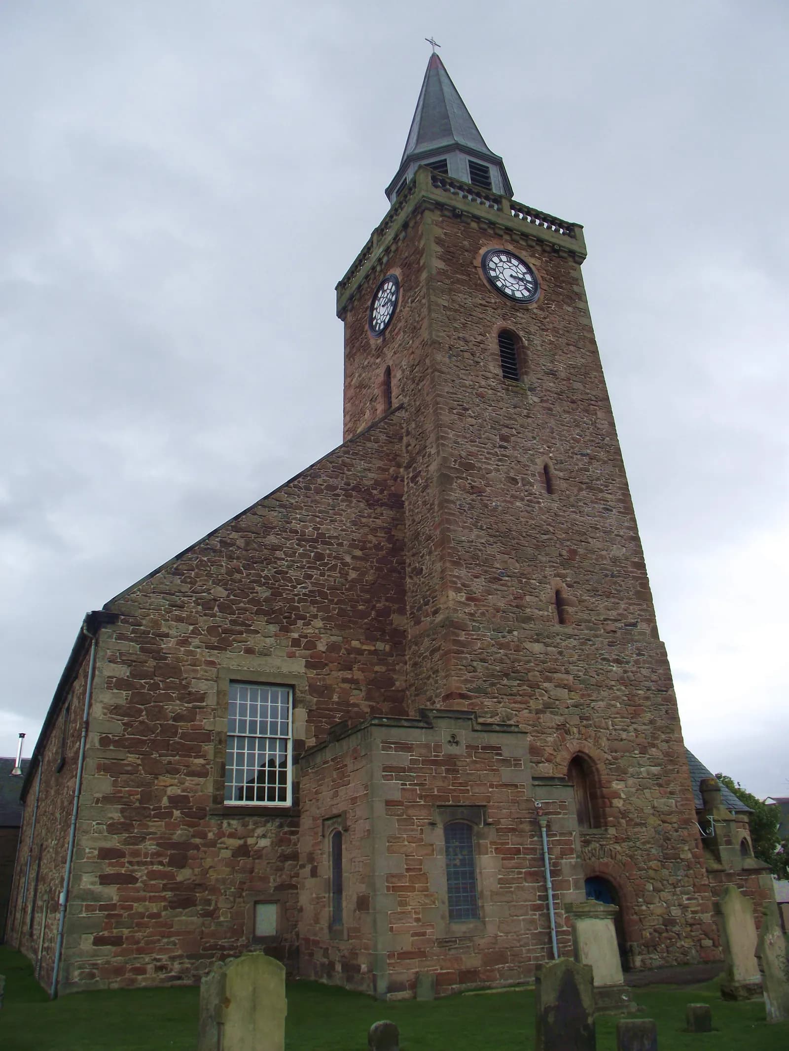 A tall, stone church with a steeple and two clock faces under a cloudy sky.