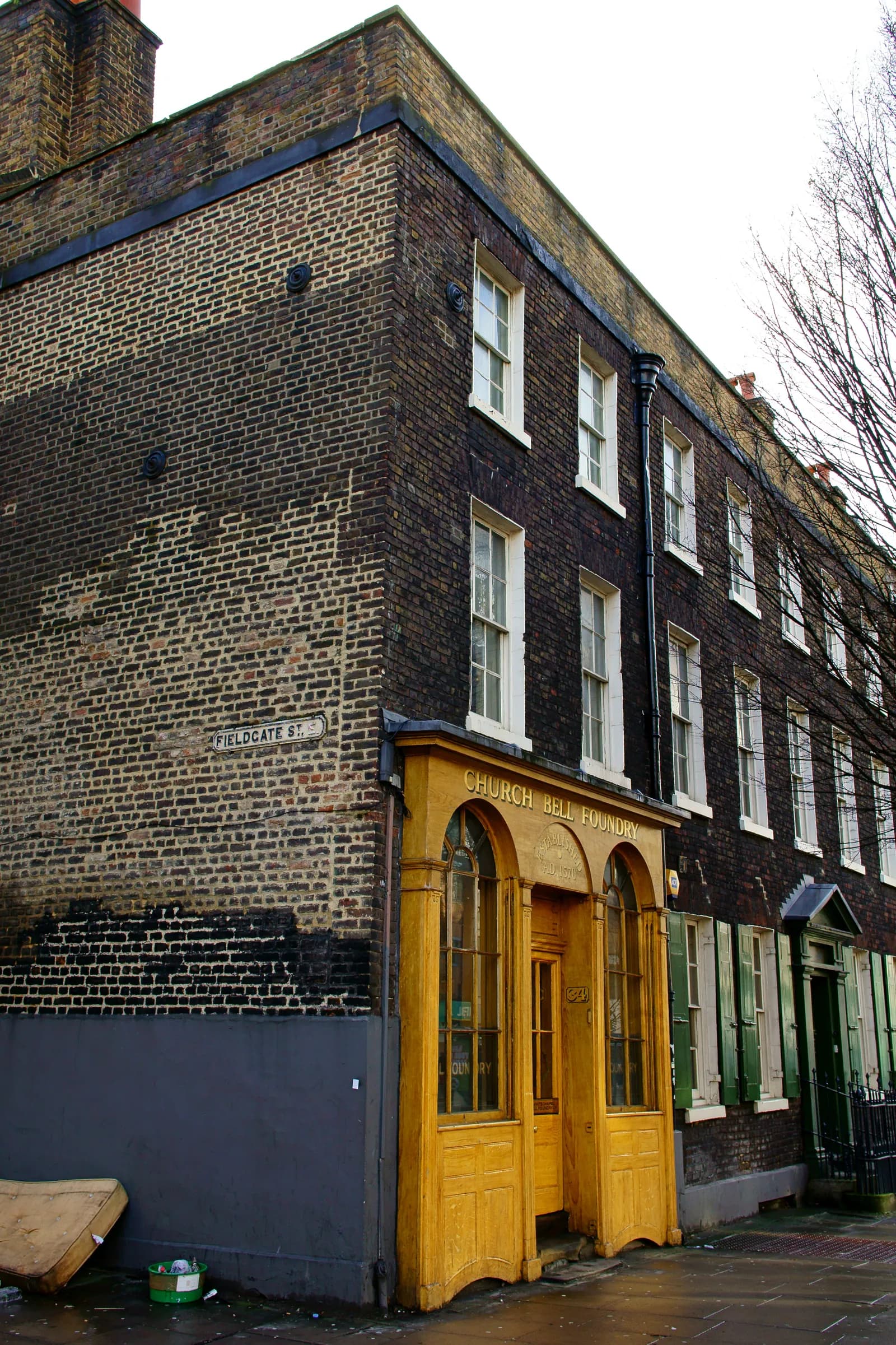 The Church Bell Foundry building on Fieldgate Street has a dark brick exterior with an ornate golden wooden facade featuring arched windows and a doorway, contrasting with the adjacent simpler brick wall.