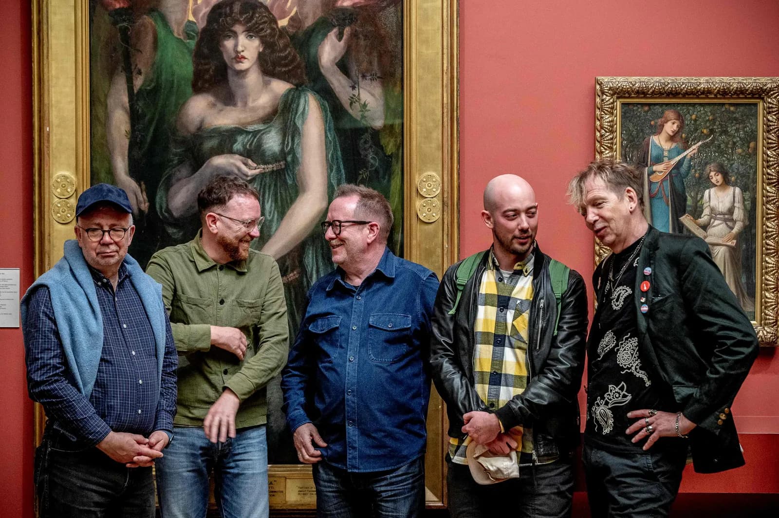Five men standing and talking in front of paintings in an art gallery.