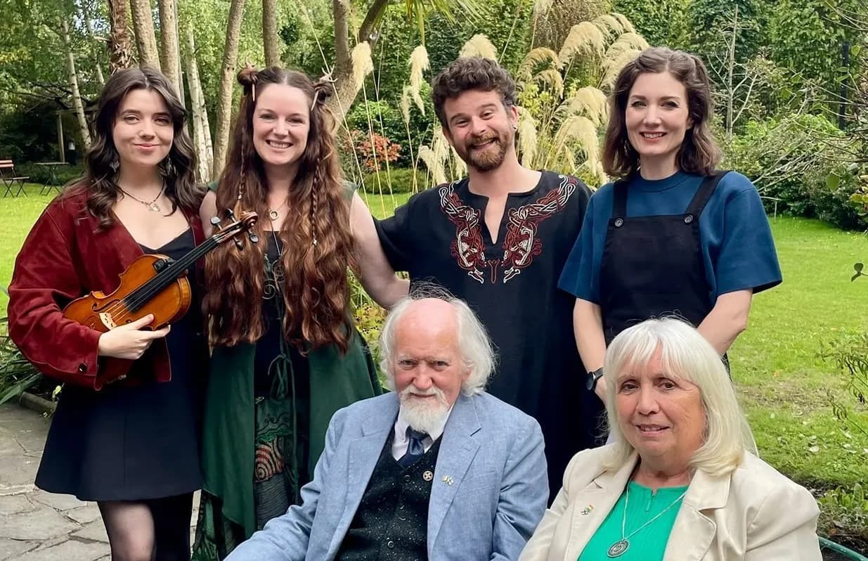 A group of six people, some young and some older, smiling at the camera in a lush green garden setting.