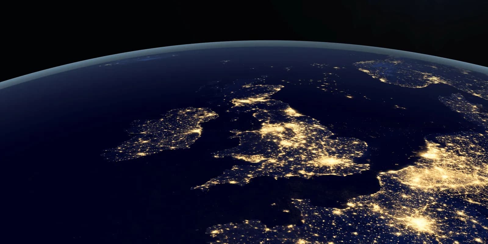 Satellite view of Europe at night, showing the United Kingdom and Ireland brightly lit with city lights, particularly dense in England, against the dark ocean and continent.