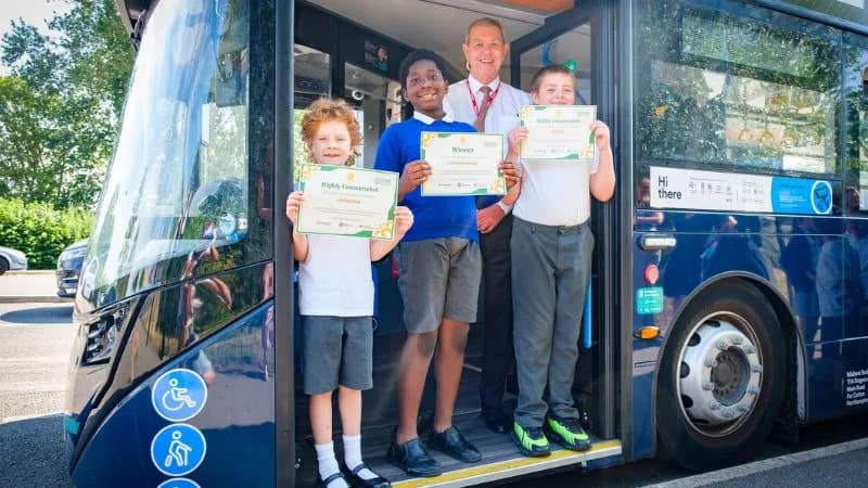 A man in a tie stands with three young boys on a bus, all holding certificates and smiling.