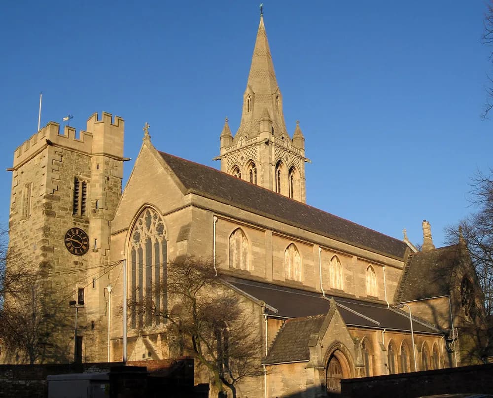 A historic stone church under a clear blue sky, featuring a tall spire and a square clock tower with battlements.
