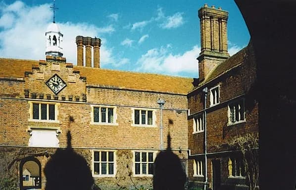 A close-up view of an old red brick building with many rectangular windows, a clock, and a bell tower on the roof under a blue sky with white clouds.