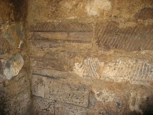 Detailed view of an ancient wall with carved geometric patterns and textured stone surfaces, possibly in an archaeological site.
