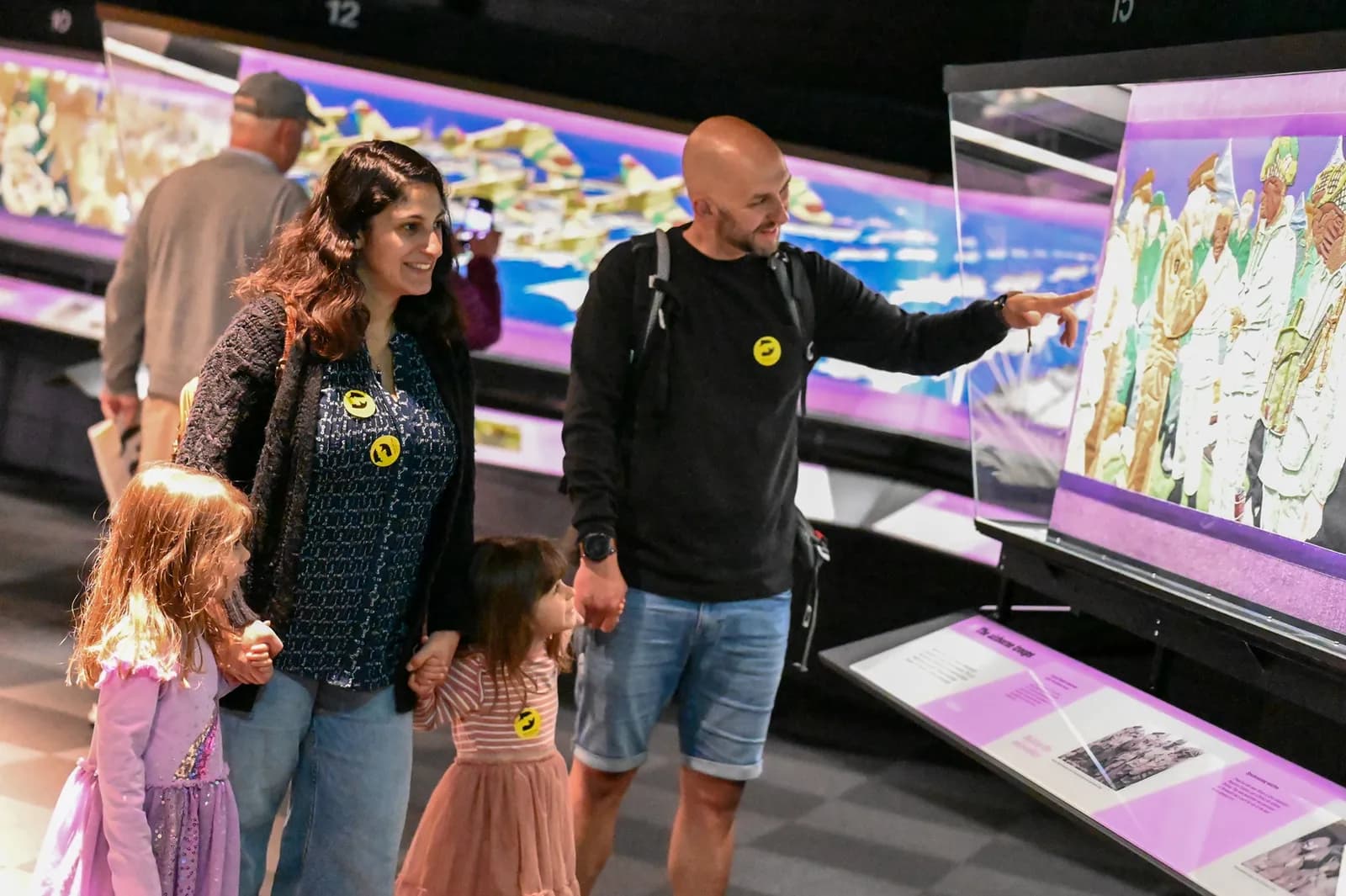 A family consisting of two adults and two young girls are looking at an exhibition at a museum.
