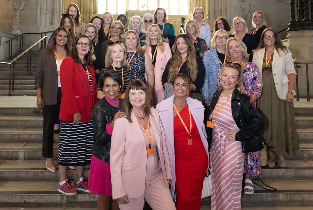 A large group of women of diverse ages are posing for a photo on a wide set of stairs, looking directly at the camera and smiling.