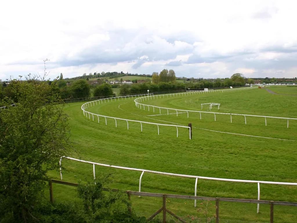 A sweeping view of a green racetrack with white fences, under a cloudy sky.