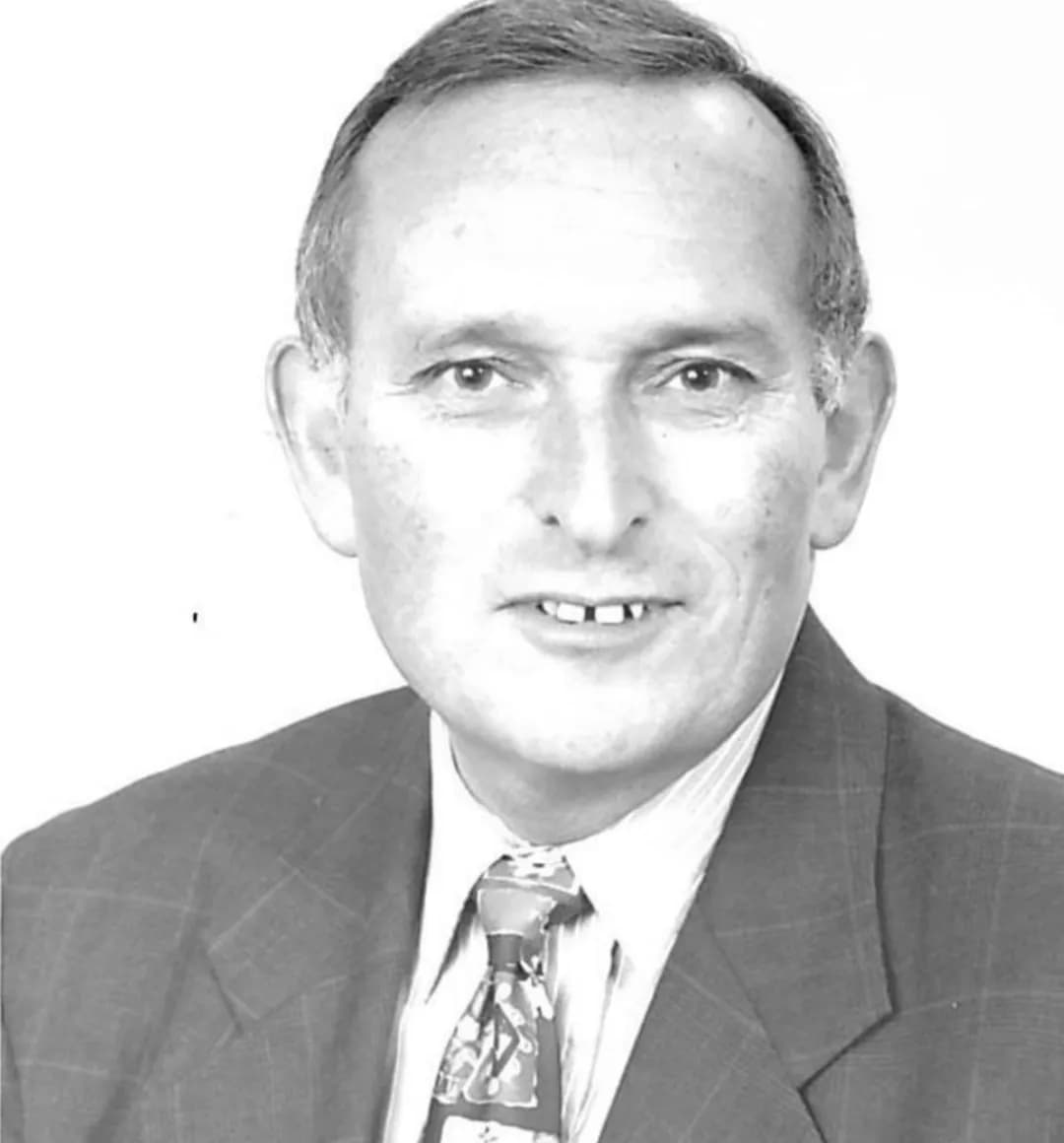 A black and white portrait of a middle-aged man wearing a suit and patterned tie, looking directly at the camera with a slight smile.