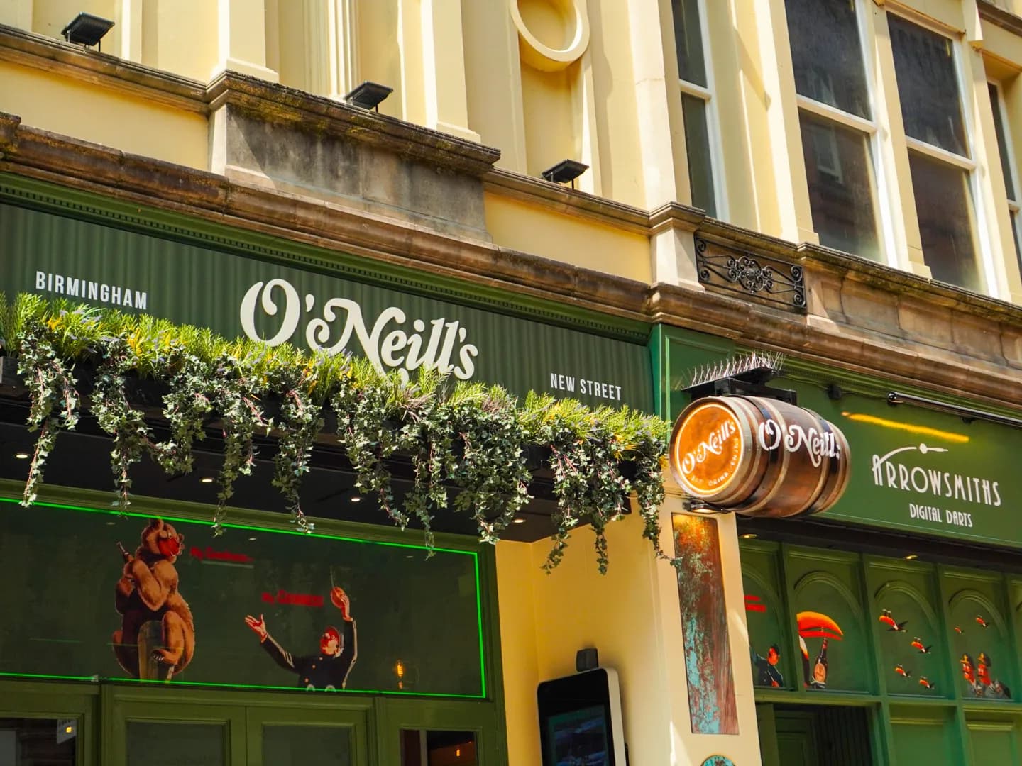 The storefront of O'Neill's pub, a bustling establishment with lush green foliage adorning its entrance, and a hanging wooden barrel sign.