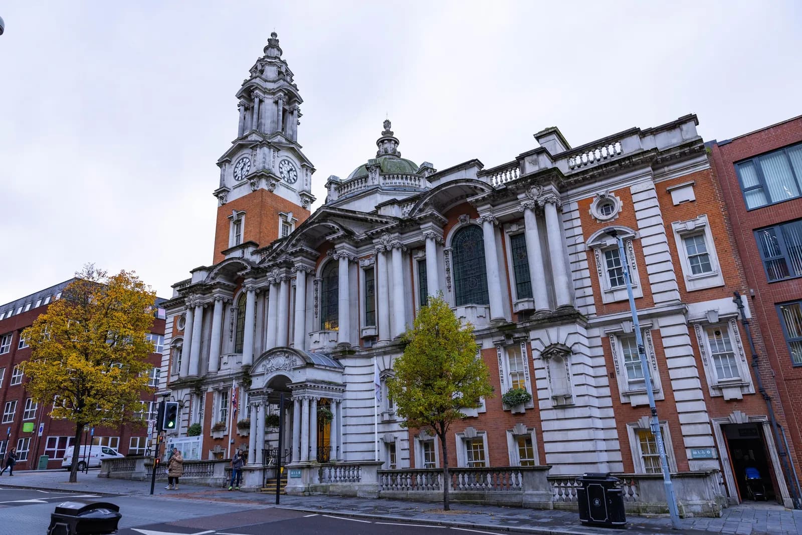 A grand, classical building with a tall clock tower and a dome, featuring ornate white stone and red brick, on a city street.