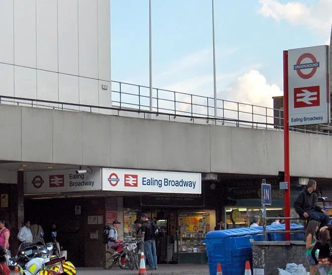 The entrance to the Ealing Broadway underground station, with its distinctive red and white signs, is visible from a street-level perspective.