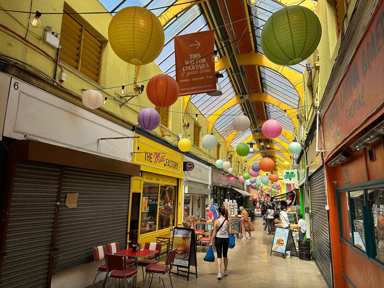 A colorful pedestrian shopping arcade with a high glass ceiling, shops on either side, and numerous round paper lanterns strung across the passageway.