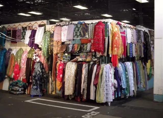A bustling market stall with racks and shelves overflowing with brightly colored garments, fabrics, and accessories.