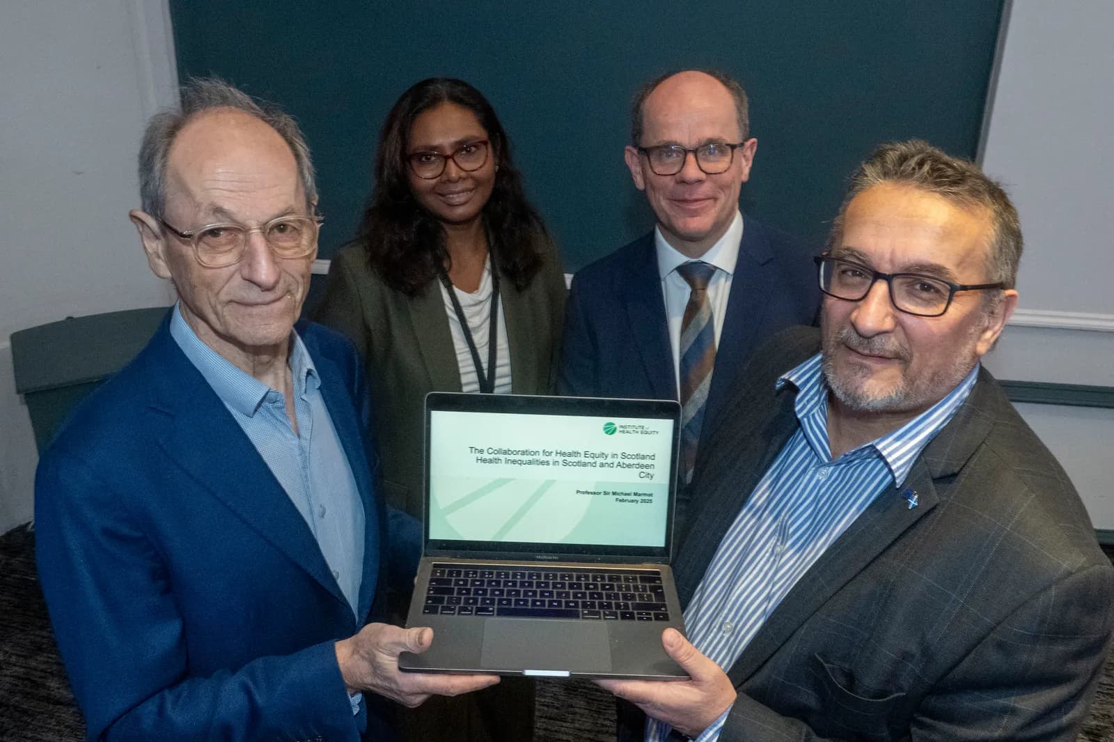 Four professionals, three men and one woman, are presenting a laptop displaying a title slide about health equity in Scotland.