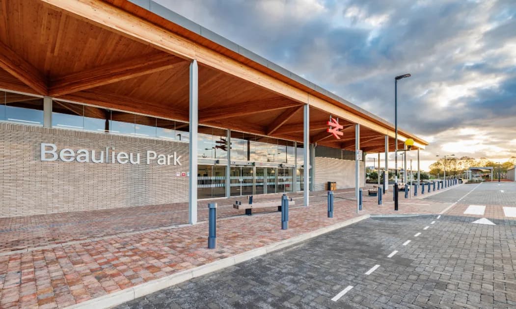 The modern Beaulieu Park train station entrance features a wooden canopy, glass doors, and a brick facade, under a cloudy sky.