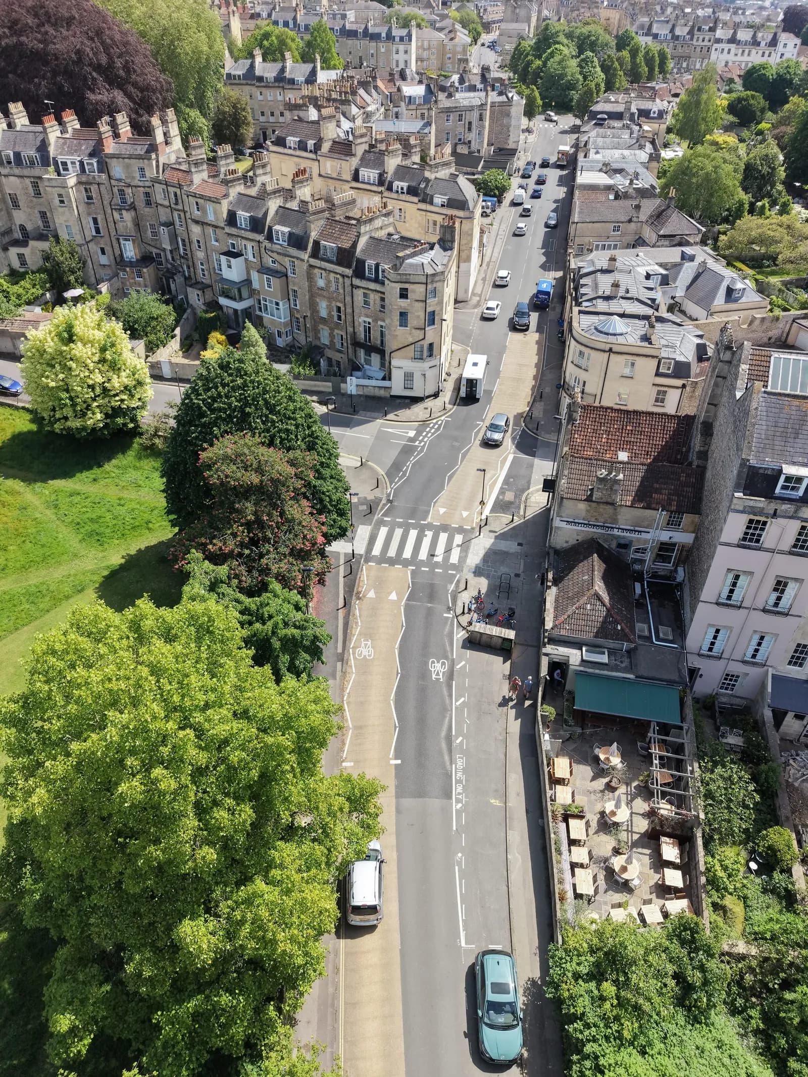 An aerial view of a busy street in an old European city, with cars, pedestrians, and historic buildings lining the road.