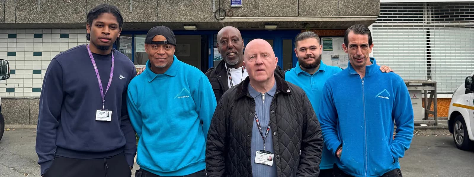 A diverse group of six men stand smiling for a picture in front of a building entrance.