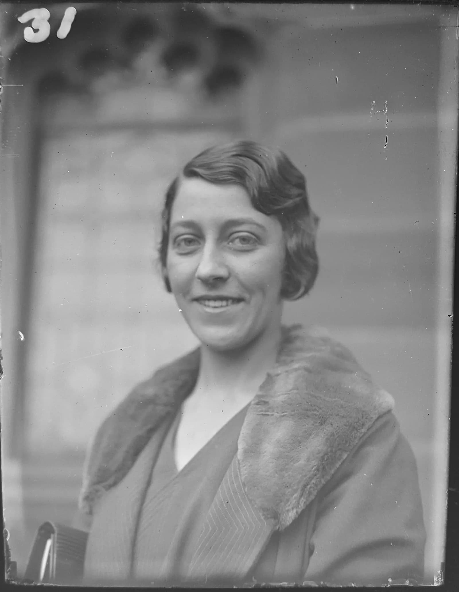 A black and white portrait of a smiling woman with wavy short hair, wearing a coat with a fur collar.