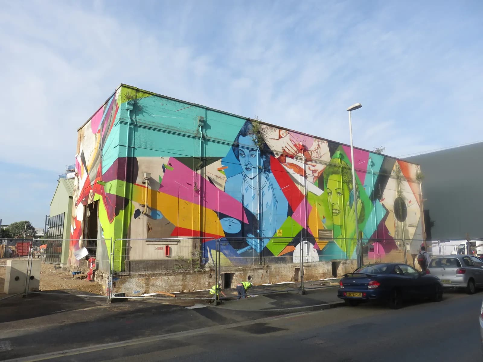 A building covered in colorful, abstract graffiti that includes an image of a man in blue and a woman in green.