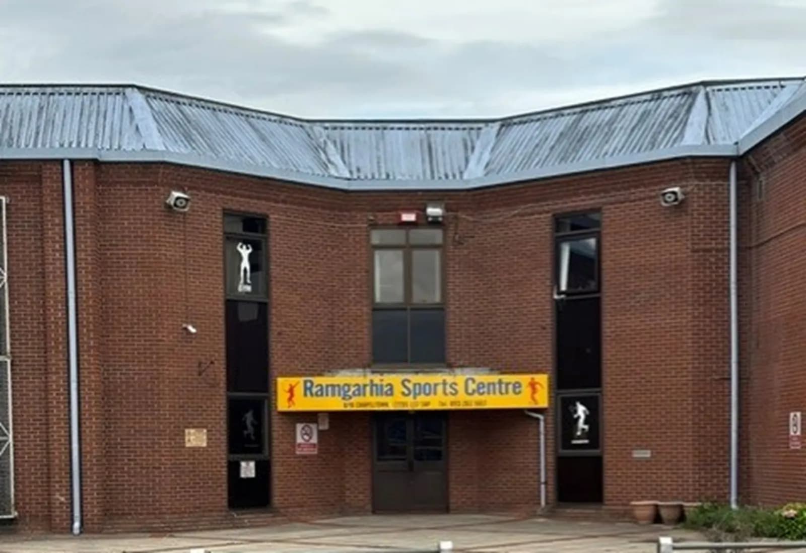 A brick building with a large yellow sign above the entrance that reads "Ramgarhia Sports Centre."