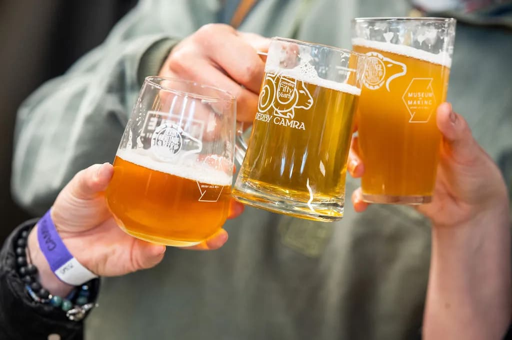 Three people holding up glasses filled with golden beer, with visible logos on the glassware.