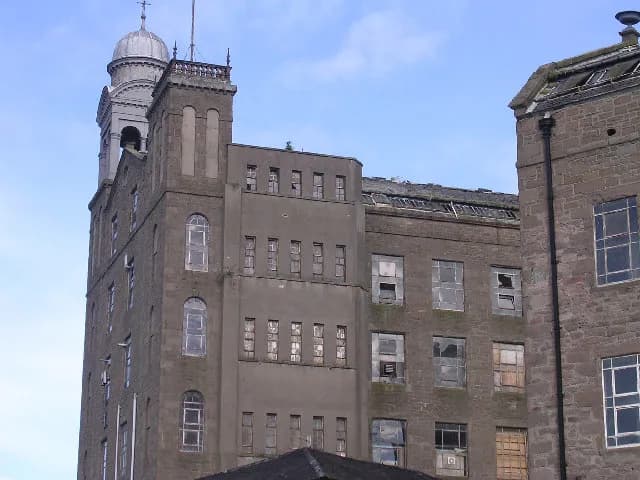 A historic, large, brick building with a dominant tower on the left, featuring a dome top, set against a partly cloudy sky.
