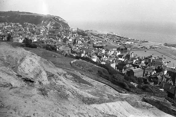 A black and white aerial view shows a densely packed town built into a hillside, with a harbor and open water visible in the background.