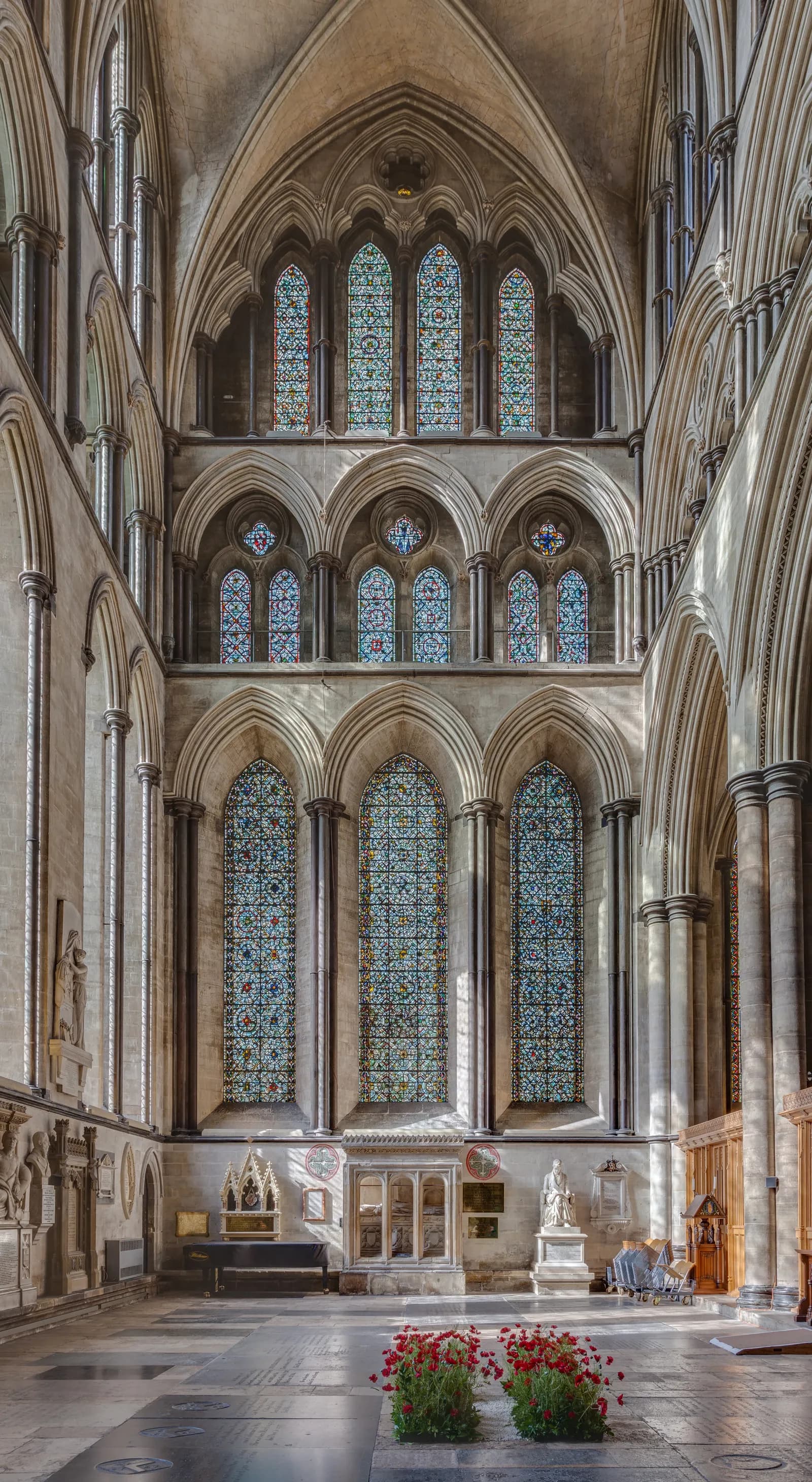 A grand, tall interior view of a cathedral with multiple levels of ornate stained-glass windows, soaring arches, and detailed stonework.