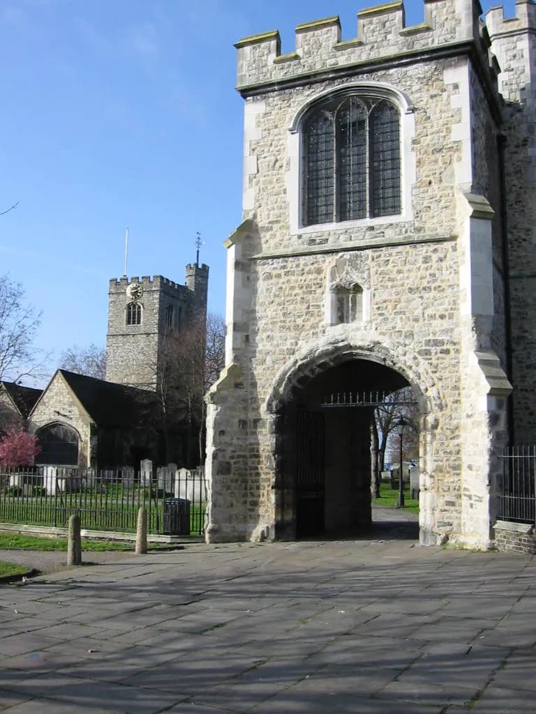 A large stone church with an arched entryway on the right, and another stone church with a clock tower in the background on the left.