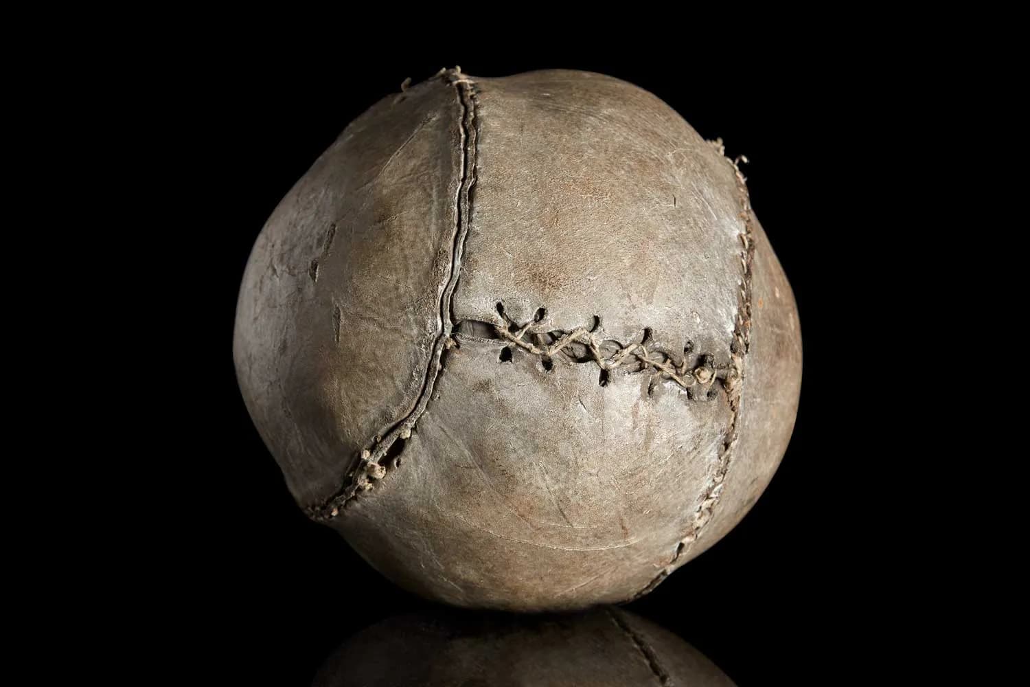 A close-up view of an antique leather football with visible stitching and a well-used texture, set against a dark background.